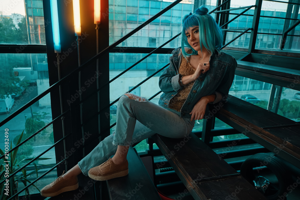 Stylish woman wearing a blue wig sitting on stairs in a modern 