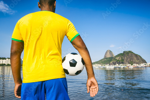 Soccer player holding football wearing shirt in Brazil flag colors at Sugarloaf in Rio de Janeiro photo