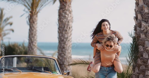 Hipster girls having fun with piggyback ride on road trip