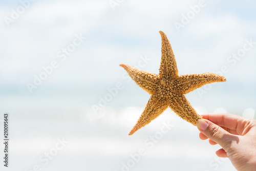 woman hand holding starfish over sea and Sandy beach in background for summer holiday and vacation concept.