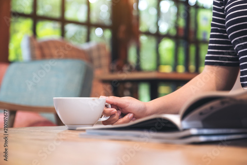 Closeup image of a woman reading a magazine while drinking coffee in cafe