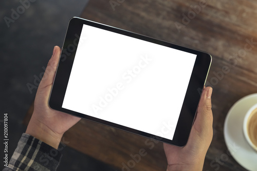 Top view mockup image of a woman holding black tablet pc with blank white desktop screen while drinking coffee in cafe
