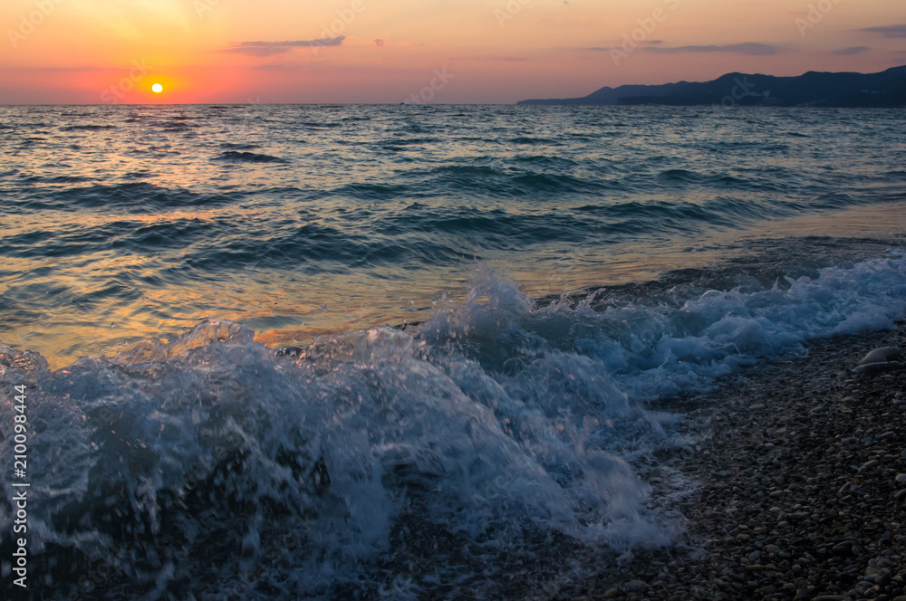 Amazing sea sunset on the pebble beach, the sun, waves, clouds