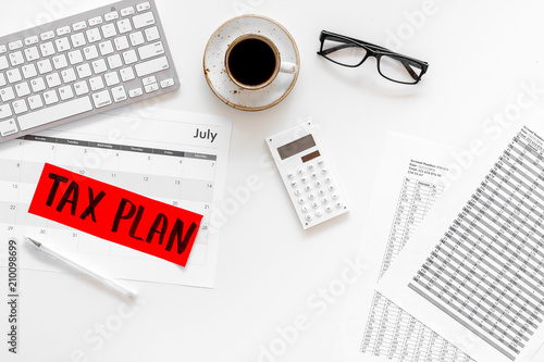 Tax plan words on office work desk with bills, keyboard, coffee, glasses on white background top view
