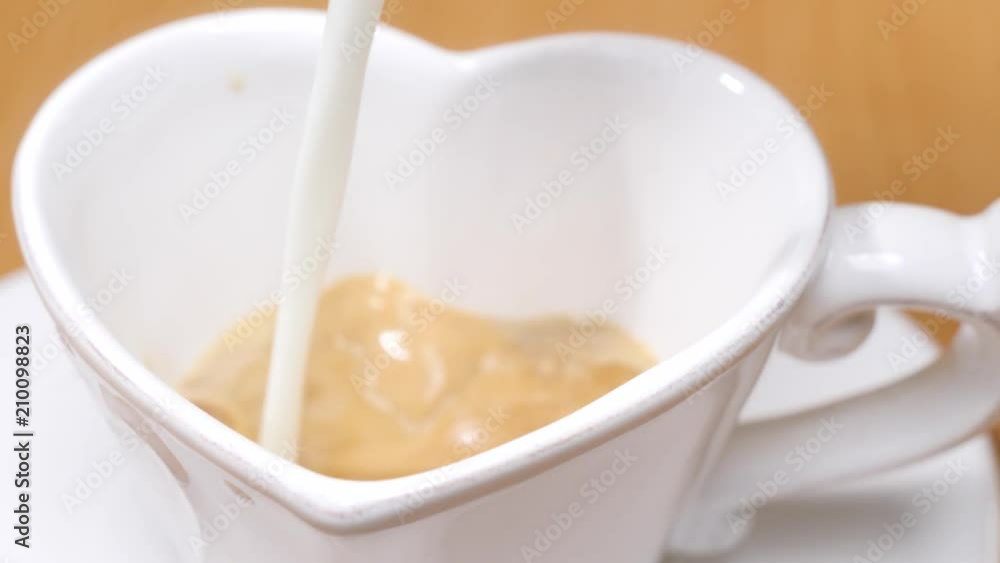 Pouring stream milk into heart shaped cup of espresso, slow motion Pouring stream milk into heart shaped cup of espresso, slow motion
