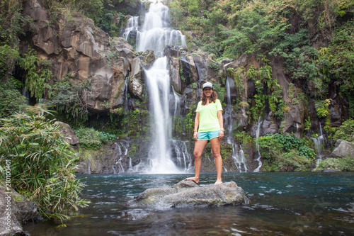 Woman model stands in front of a tropical waterfall long exposure