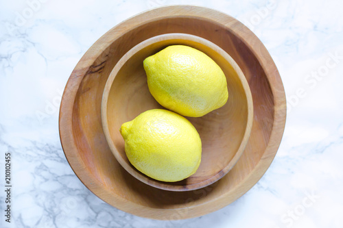 Yellow lemons in wooden bowls on a white marble background 