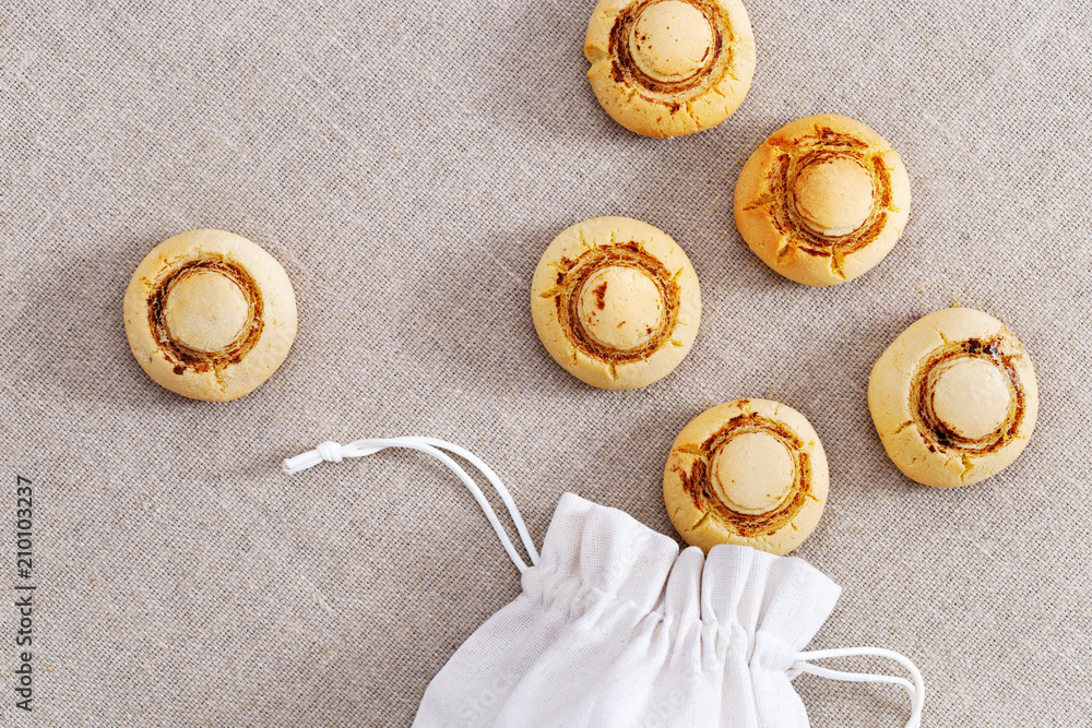 Shortbread cookies in form of champignons. Baked sweet biscuits spilled out of bag on sackcloth. Delicious dessert. Food background. Top view. Shortbread cookies in form of champignons. Baked sweet biscuits spilled out of bag on sackcloth. Delicious dessert. Food background. Top view.