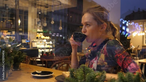 Girl drinking her espresso coffe sitting behind the glass frontage in cafe bistro, the view fromm street photo