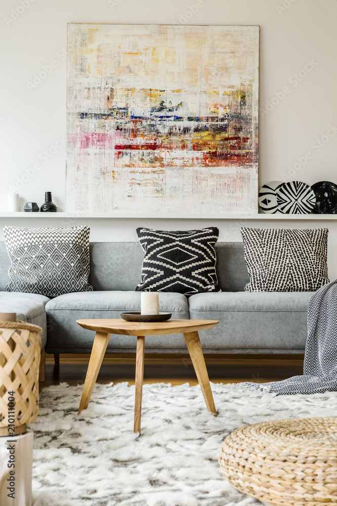 Painting above grey couch in boho living room interior with wooden table and  pouf. Real photo foto de Stock | Adobe Stock