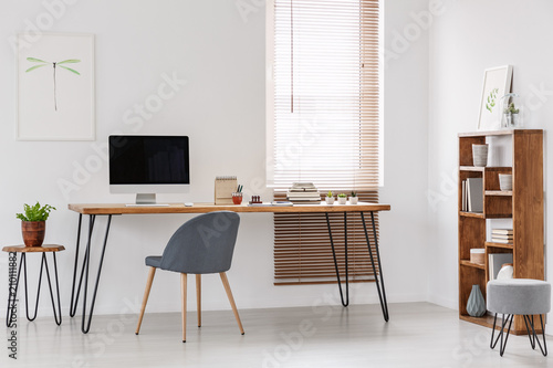 Natural and bright office of a start-up company with wooden furniture, desktop computer and gray chair at the desk. Real photo