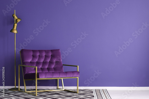Ultra violet armchair with golden details and lamp standing on the empty wall