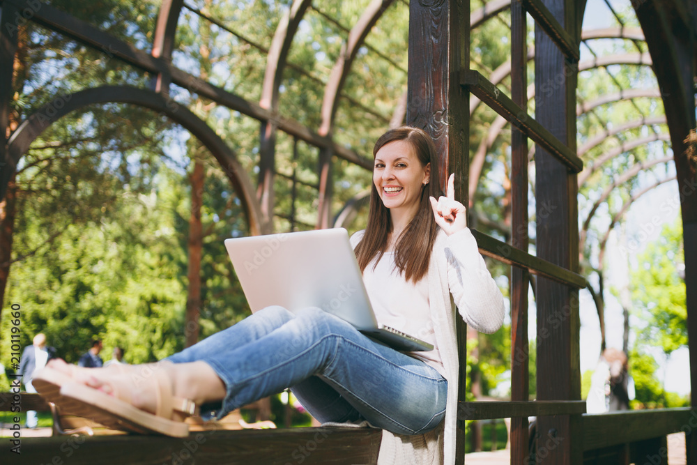 Obraz premium Young successful businesswoman in light casual clothes. Smiling Woman working on modern laptop pc computer in city park in street outdoors on spring nature. Mobile Office. Freelance business concept.