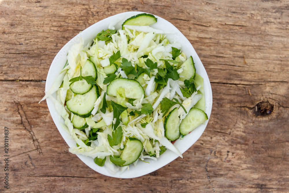 Spring vegan salad with cabbage, cucumber, green onion and parsley on wooden table. Top view Spring vegan salad with cabbage, cucumber, green onion and parsley on wooden table. Top view