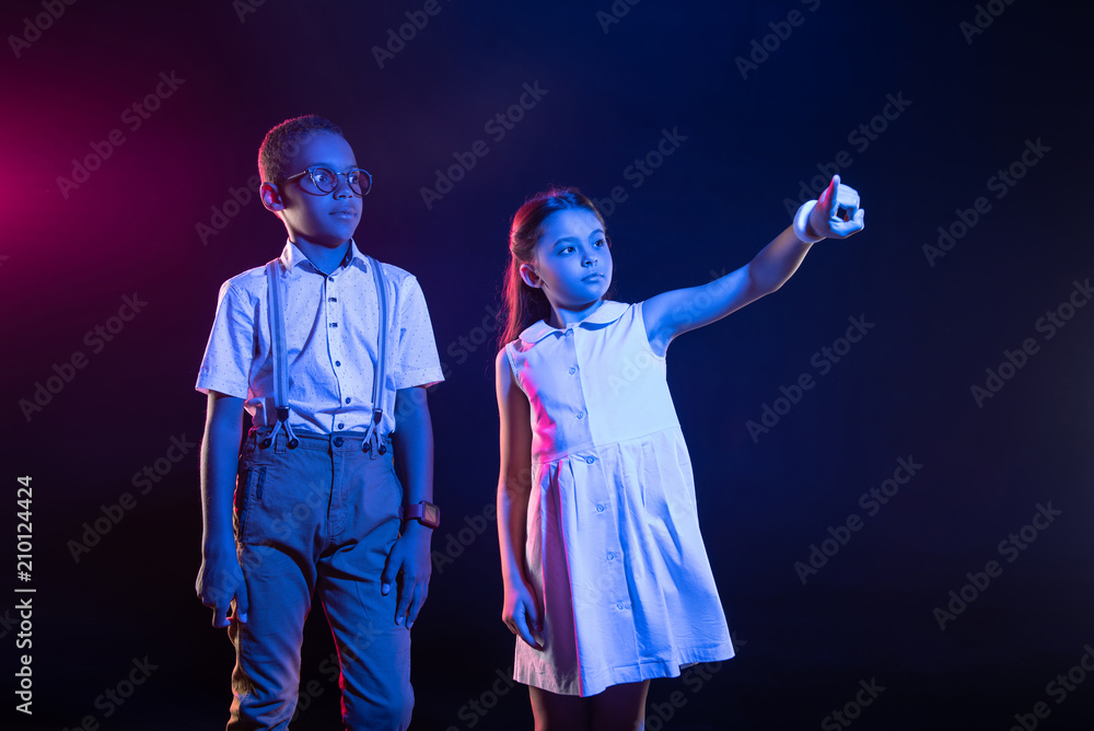 Our imagination. Content cute girl pressing imaginary buttons and the boy standing near her