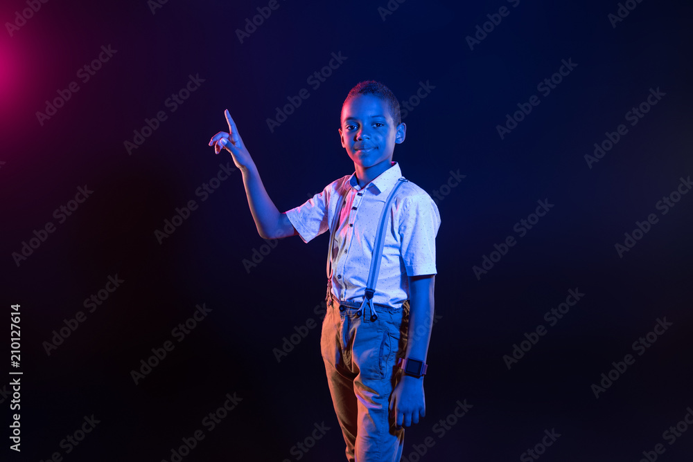 Joyfulness. Alert dark-eyed boy pressing some buttons and smiling while standing Joyfulness. Alert dark-eyed boy pressing some buttons and smiling while standing