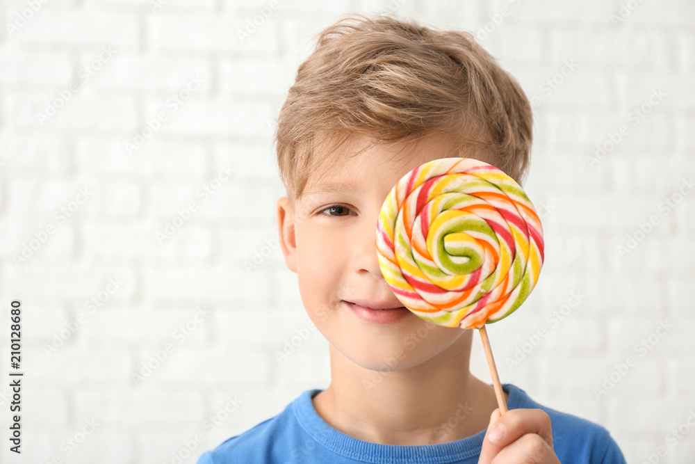 Cute little boy with lollipop near white brick wall