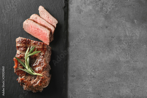 Slate plate with tasty grilled steak on grey background
