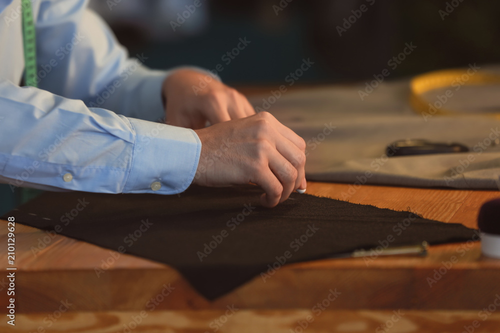 Young tailor marking fabric with chalk in atelier