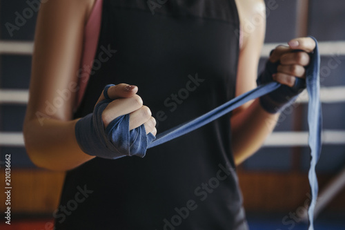 Woman bandage her hands before box sparring on a ring in gym. Close up of her hands