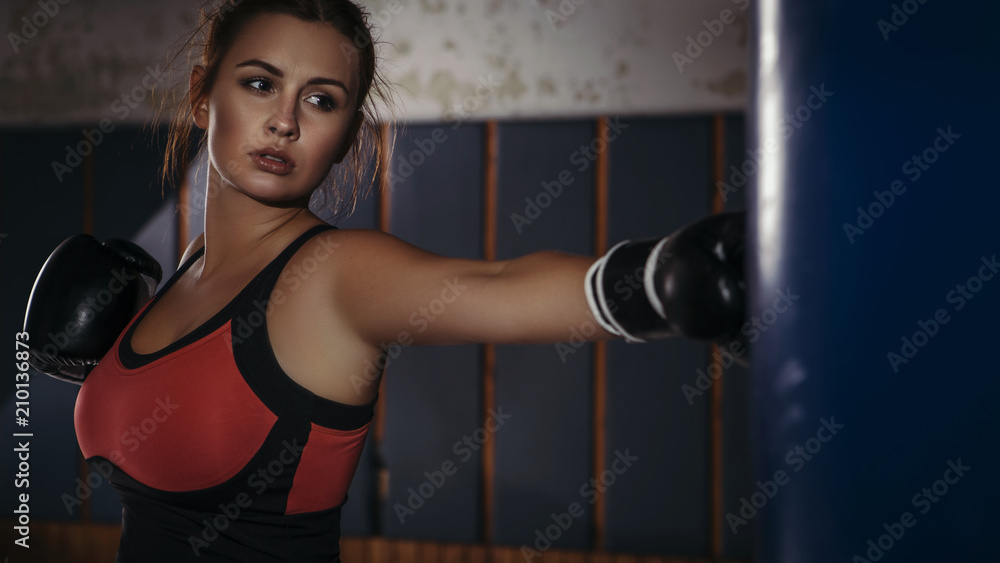 Fit slim young beautiful brunette woman boxing in sportswear. Dark dim light. Toned image