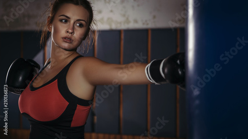 Fit slim young beautiful brunette woman boxing in sportswear. Dark dim light. Toned image © AnnaDemy
