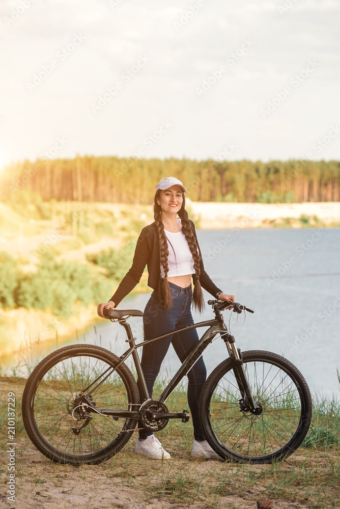 The beautiful girl is standing by bicycle. Senior woman riding a bike beside a lake. A female biker take a rest after biking The beautiful girl is standing by bicycle. Senior woman riding a bike beside a lake. A female biker take a rest after biking