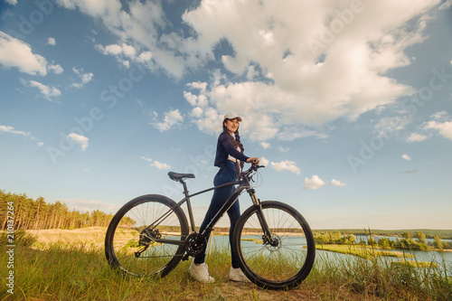 The beautiful girl is standing by bicycle. Senior woman riding a bike beside a lake. A female biker take a rest after biking