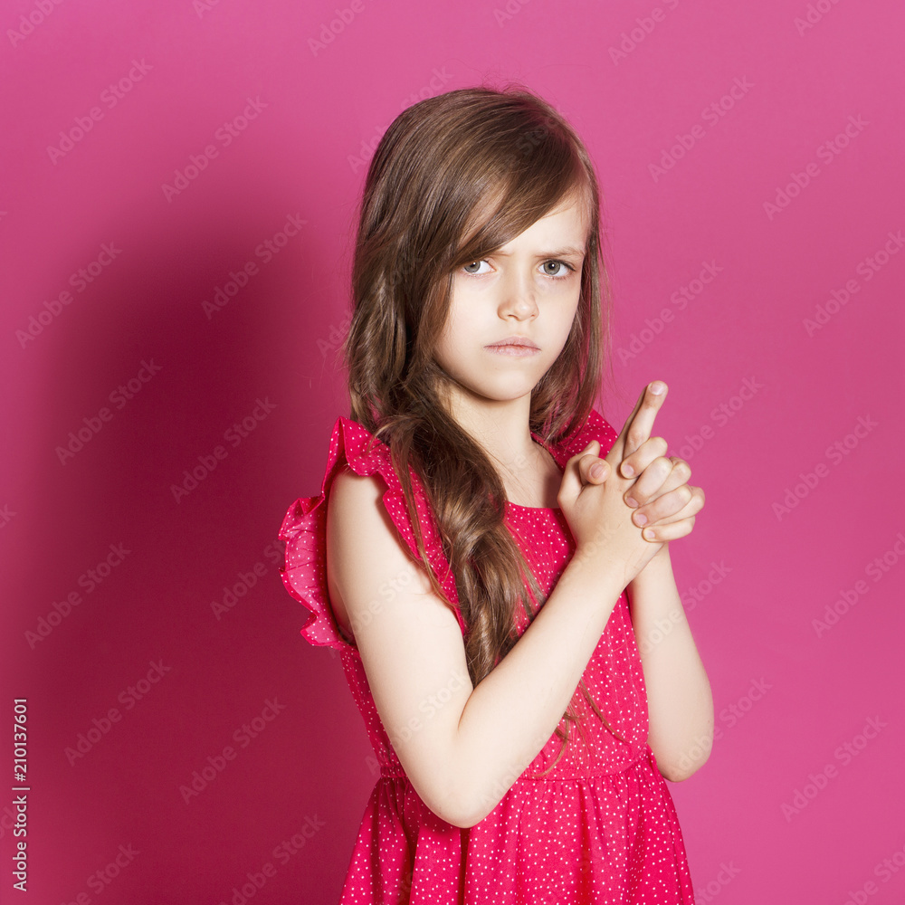 Little 8 years old girl make some emotional gesture with her hands on a pink neutral background. She has long brunette hair and wear red summer dress. Funny expression on her face Little 8 years old girl make some emotional gesture with her hands on a pink neutral background. She has long brunette hair and wear red summer dress. Funny expression on her face