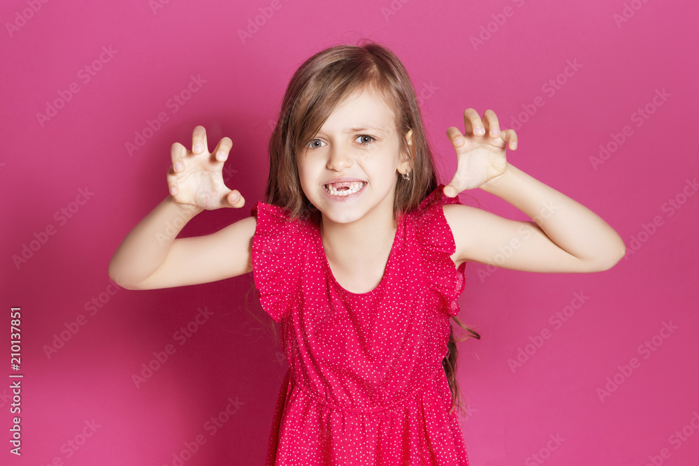 Little 8 years old girl make some emotional gesture with her hands on a pink neutral background. She has long brunette hair and wear red summer dress. Funny expression on her face Little 8 years old girl make some emotional gesture with her hands on a pink neutral background. She has long brunette hair and wear red summer dress. Funny expression on her face