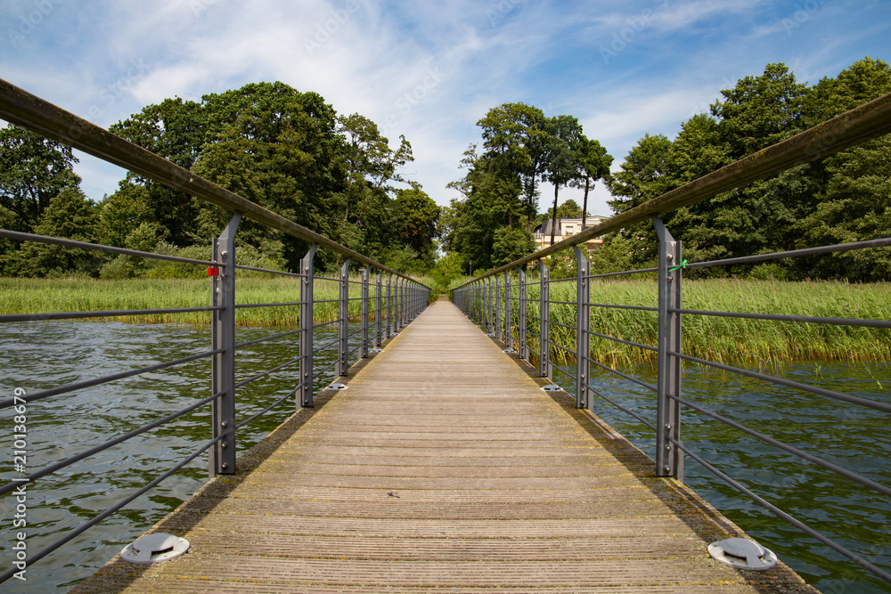 Fototapeta premium Holzbrücke über wasser mit leicht bewöltem Himmel und Bäumen