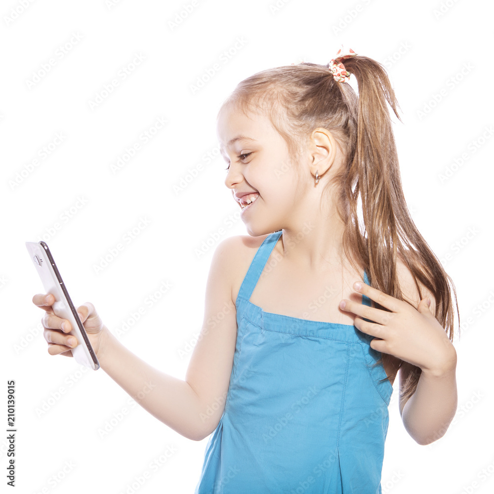 Young seven years old brunette girl in blue dress on a white isolated background. She makes selfie on her mobile phone, fun and smile emotions on her face Young seven years old brunette girl in blue dress on a white isolated background. She makes selfie on her mobile phone, fun and smile emotions on her face