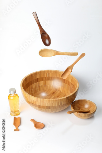 Wooden bowl spoon utensils oil bottle on white background elevated flying floating