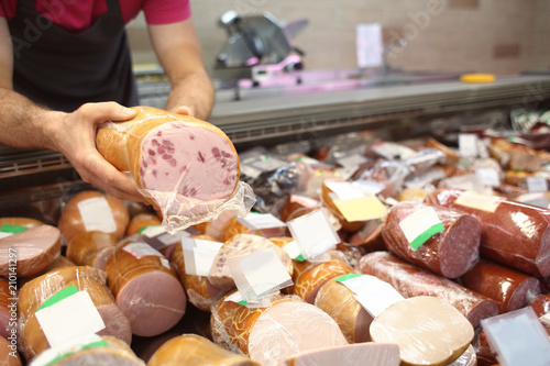 Male seller holding piece of deli meat in butcher shop photo
