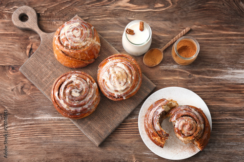 Plate and board with tasty cinnamon buns on wooden table