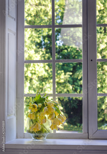 Yellow bouquet of tulips in glass jug on windowsill by window. Flowers in interior design. Cozy home.