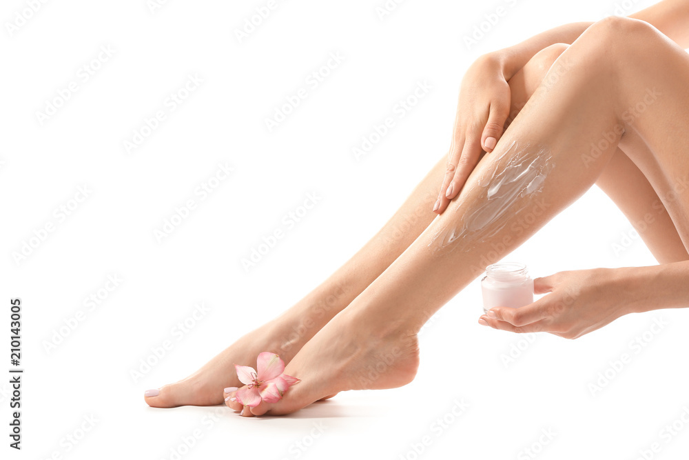 Young woman applying cream onto her leg after depilation on white background