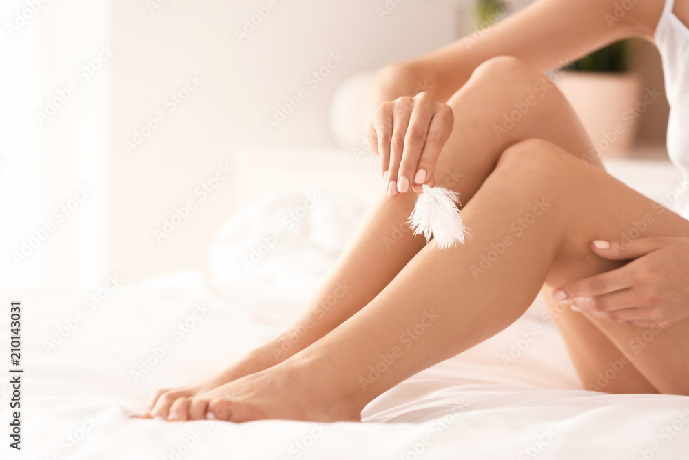 Young woman sitting on bed and showing silky skin after epilation