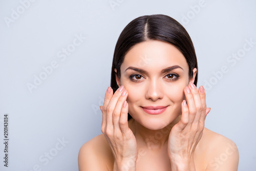 Natural nude charming woman applying lotion cream on cheekbones for flawless smooth soft skin, perfection anti-aging enhancement concept, isolated on grey background, copy space, empty place