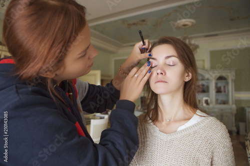 Brunette make up artist woman applying make up for a caucasian brunette bride  preparing her for a wedding photosession or a date