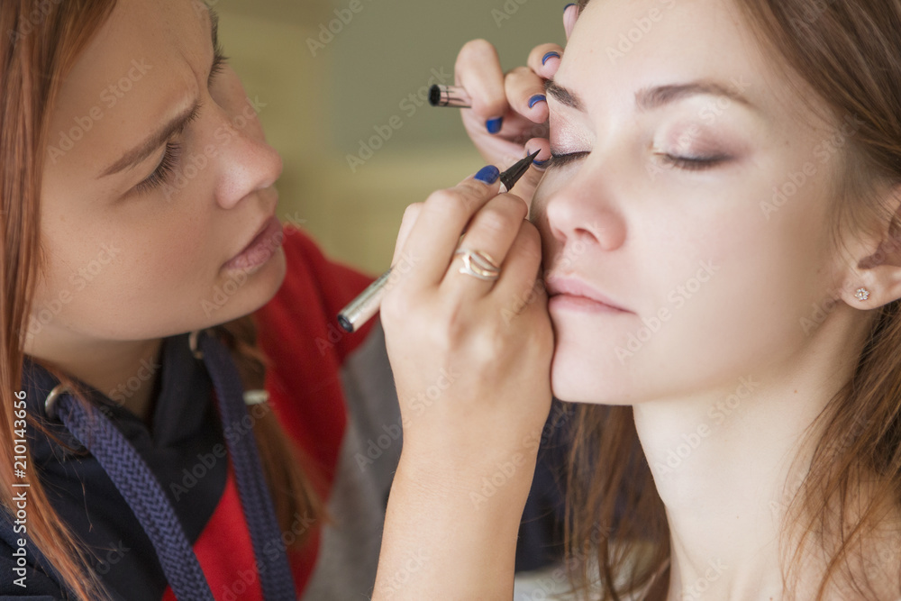 Brunette make up artist woman applying make up for a caucasian brunette bride, preparing her for a wedding photosession or a date