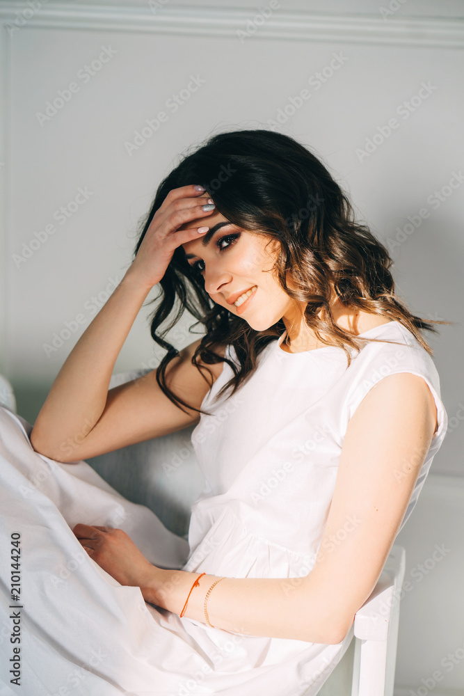 Portrait of beautiful brunette sitting in a white dress. Vertical orientation. Portrait of beautiful brunette sitting in a white dress. Vertical orientation.