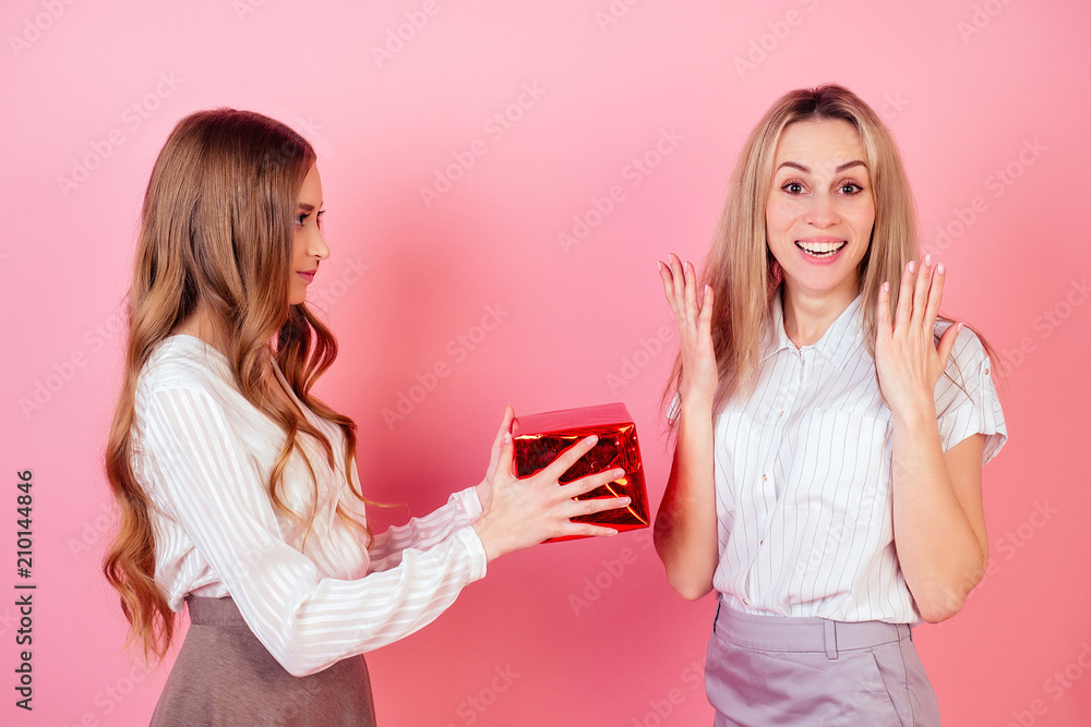 cute and young teenager girl giving box with a gift to surprised delight mom on a pink background in the studio. the concept of celebrating the mother's day and birthday cute and young teenager girl giving box with a gift to surprised delight mom on a pink background in the studio. the concept of celebrating the mother's day and birthday