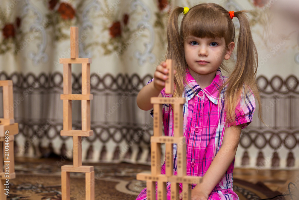 Little girl play with wooden blocks. Kid inspecting wooden block buildings, childhood activities. Tower stack from wooden blocks toy and girl's hand take one block