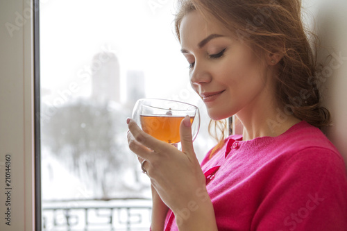 Beautiful lady woman in casual outfit standing in her luxury interior home, drinking tea from a mug. Cheerful smile on her face