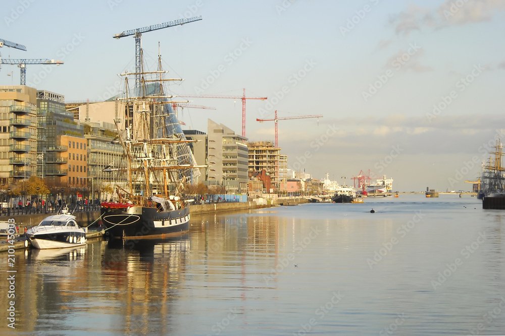 ships (yachts, schooners, ocean liners) moored in the harbor of Dublin (Ireland); many buildings under construction in the seaport