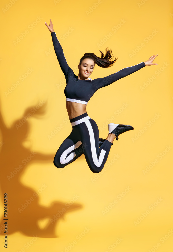 Sporty smiling woman jumping up in silhouette on yellow background. Dynamic movement. Sport and healthy lifestyle