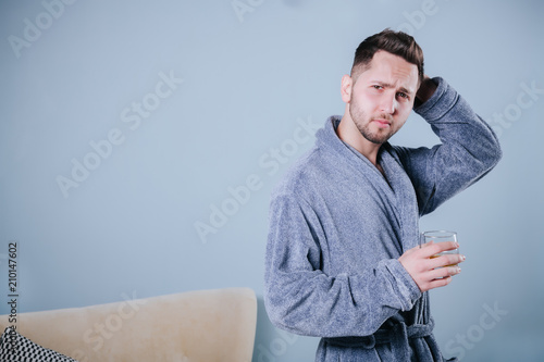 Portrait of handsome young man holding glass of cognac.Portrait of a handsome bearded Businessman in grey bathrobe drinking a Whiskey © ZoomStudio