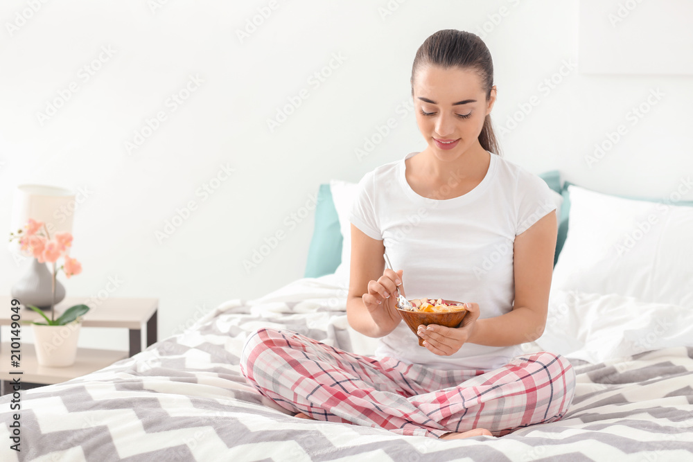 Beautiful young woman eating tasty oatmeal for breakfast in bedroom Beautiful young woman eating tasty oatmeal for breakfast in bedroom