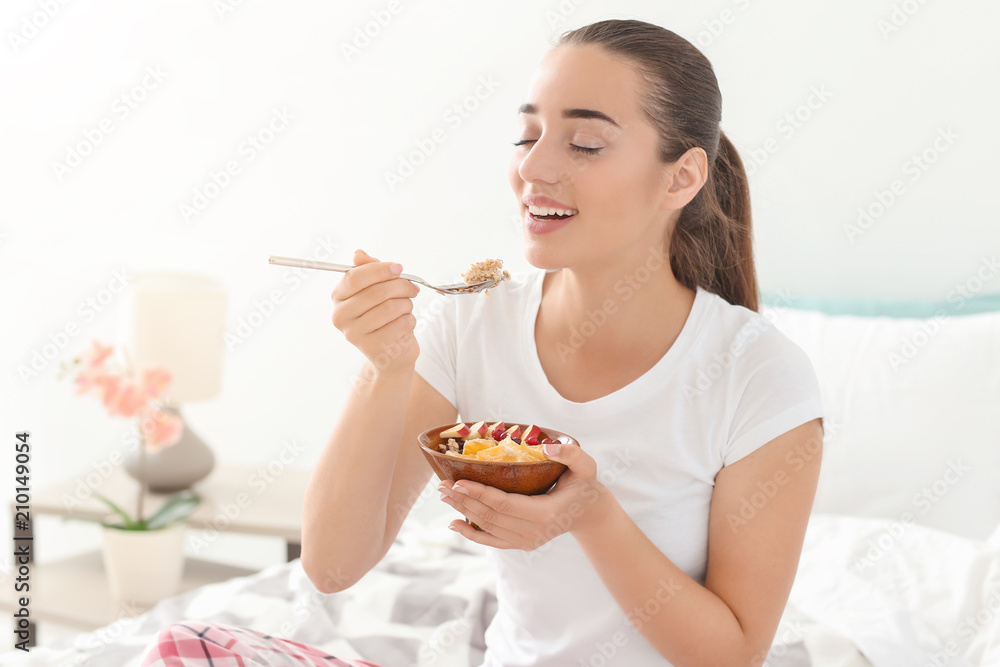 Beautiful young woman eating tasty oatmeal for breakfast in bedroom Beautiful young woman eating tasty oatmeal for breakfast in bedroom